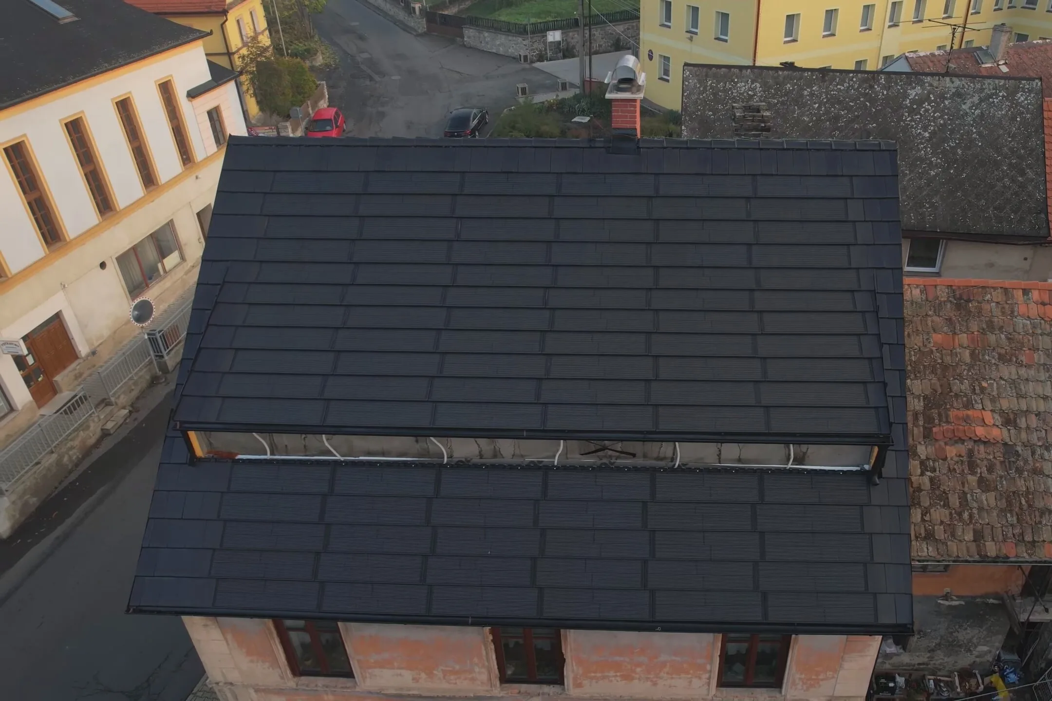 Letecký pohled na rodinný dům se střechou osazenou fotovoltaickými taškami, které vizuálně dokonale splývají s běžnou krytinou.