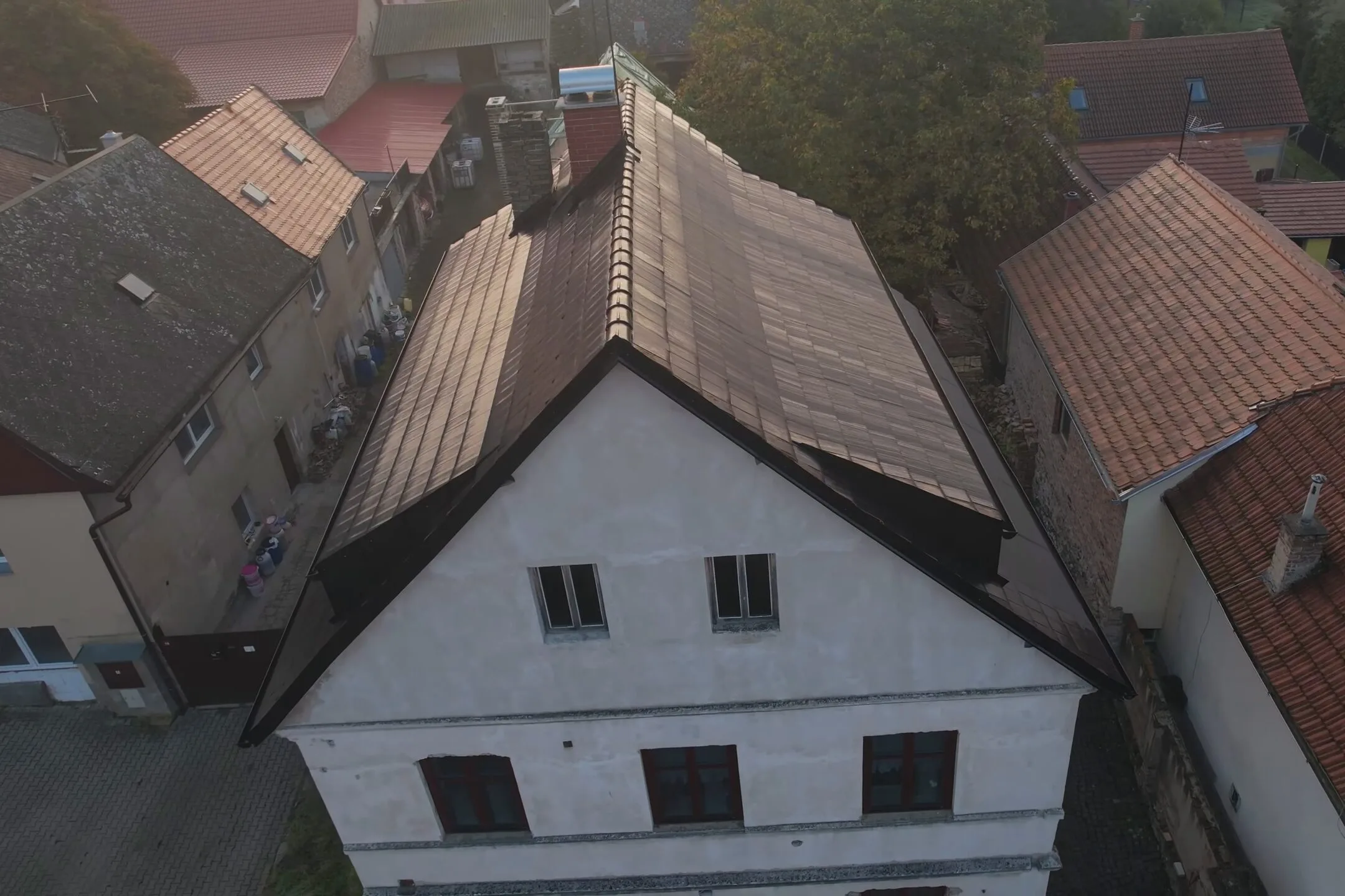 Letecký pohled na rodinný dům se střechou osazenou fotovoltaickými taškami, které vizuálně dokonale splývají s běžnou krytinou.