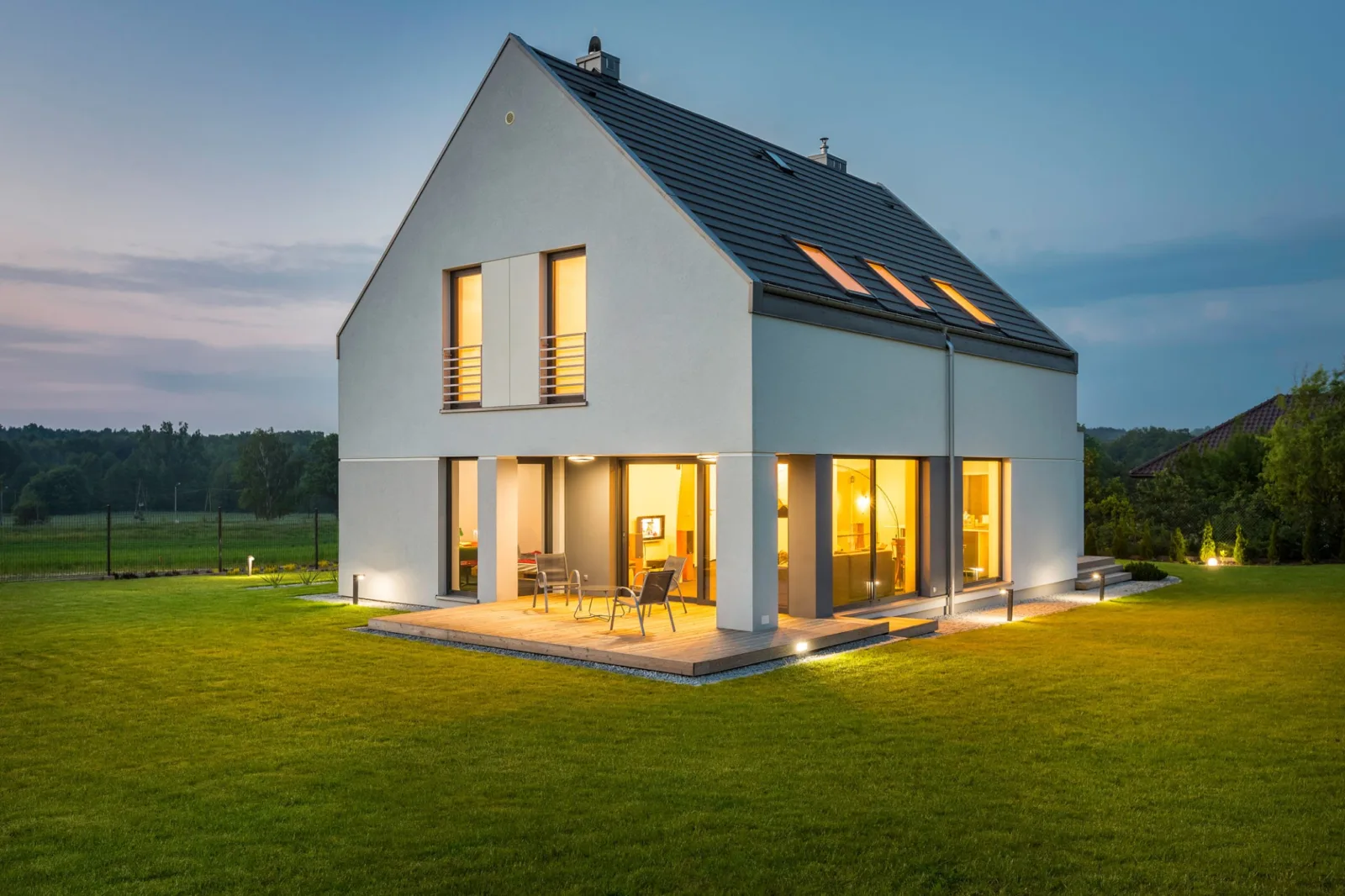 Moderní, energeticky nezávislý rodinný dům se solární střechou, svítící do podvečerní krajiny.